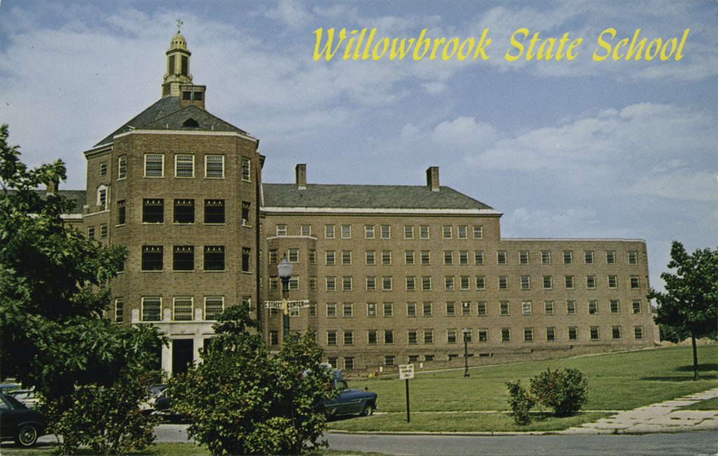 postcard showing a large red brick building within a courtyard. Text on top against a blue sky says Willowbrook State School 