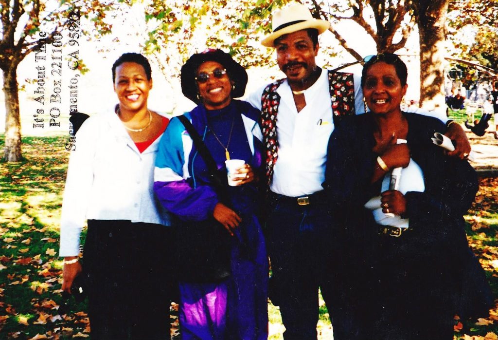 Three Black women: Patsy Combs, Norma (Armour) Mtume, and Joan Self along with a Black male Panther who is unnamed standing in front of a grassy background. Photo is stamped with text that reads: It’s About Time, PO Box 22100, Sacramento, California 95822. 