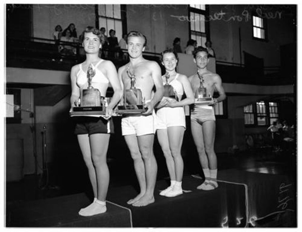 Four teenagers--two female and two male, stand in good posture, smiling. They are all holding trophies. 