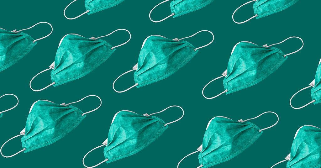 Green surgical masks with white earloops are situated in rows across a darker green background.
