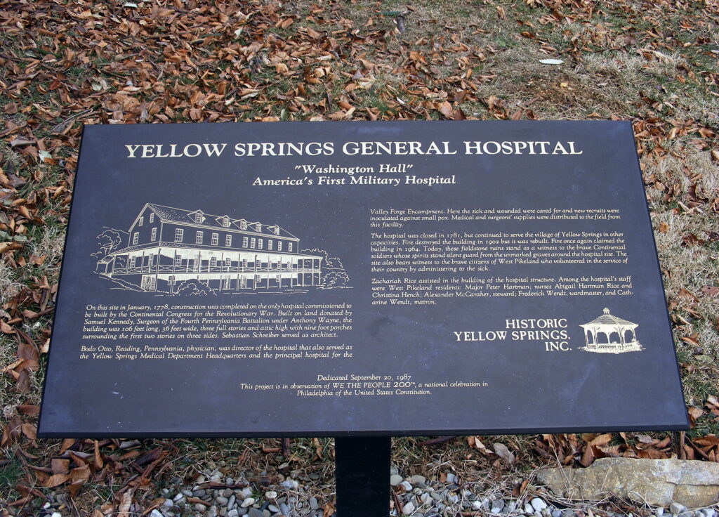 Pictured if a black rectangular plaque with light yellow text describing the significance of America's first military hospital Yellow Springs General Hospital or, as similarly recognized, "Washington Hall."