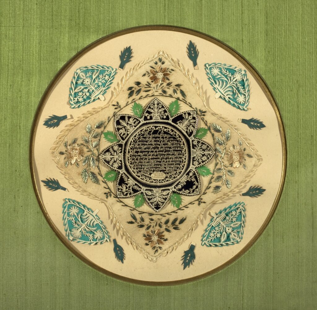 Circular paper cut out with a leaf motif with the Lord's Prayer in the center.