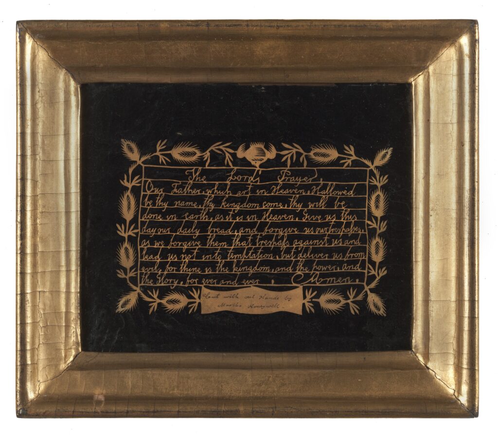 Beige cut out on a black background of the Lord's Prayer surrounded by a leaf motif with the caption "Cut with out Hands by Martha Honeywell"